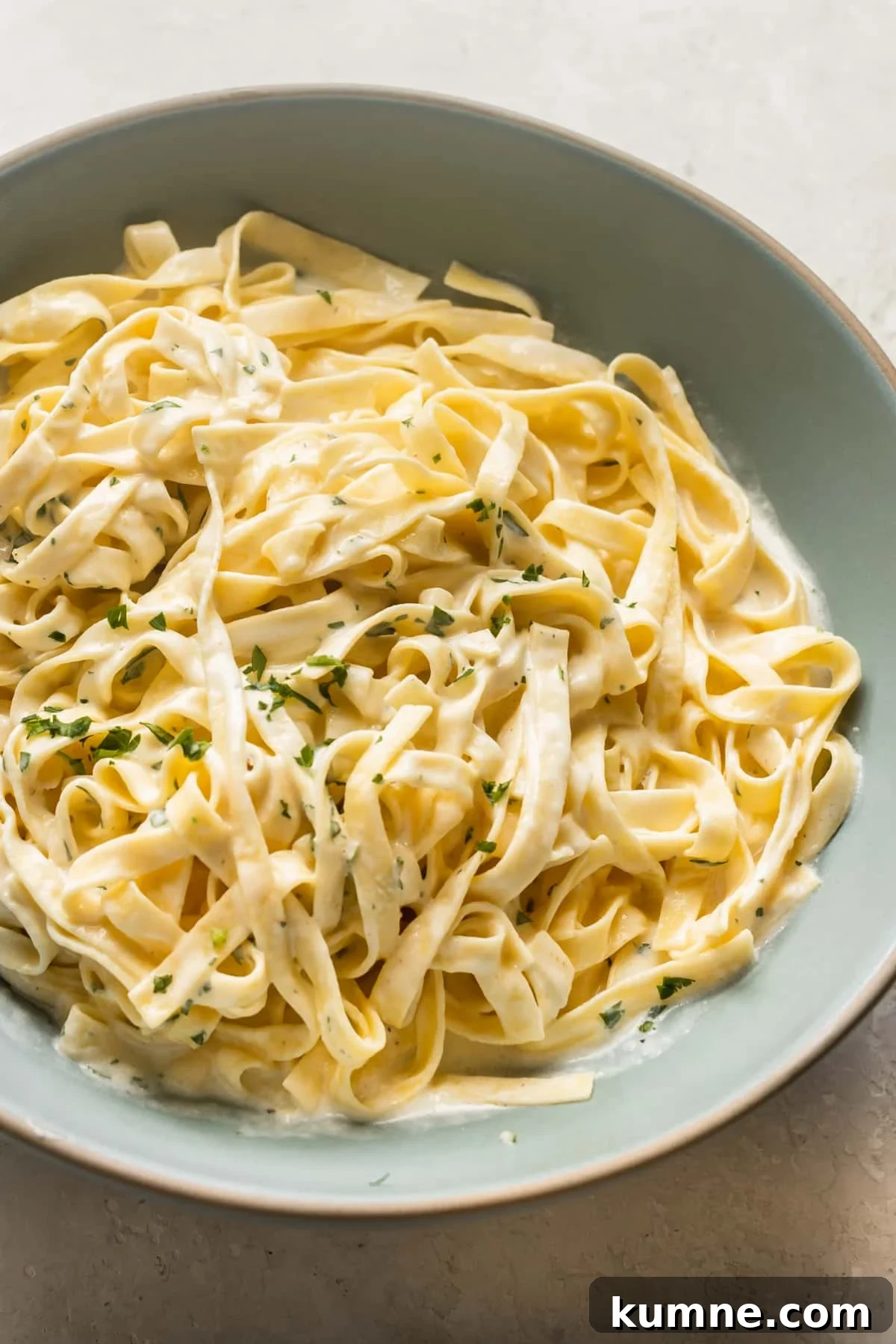 fettuccine pasta tossed with Alfredo sauce in a blue bowl.