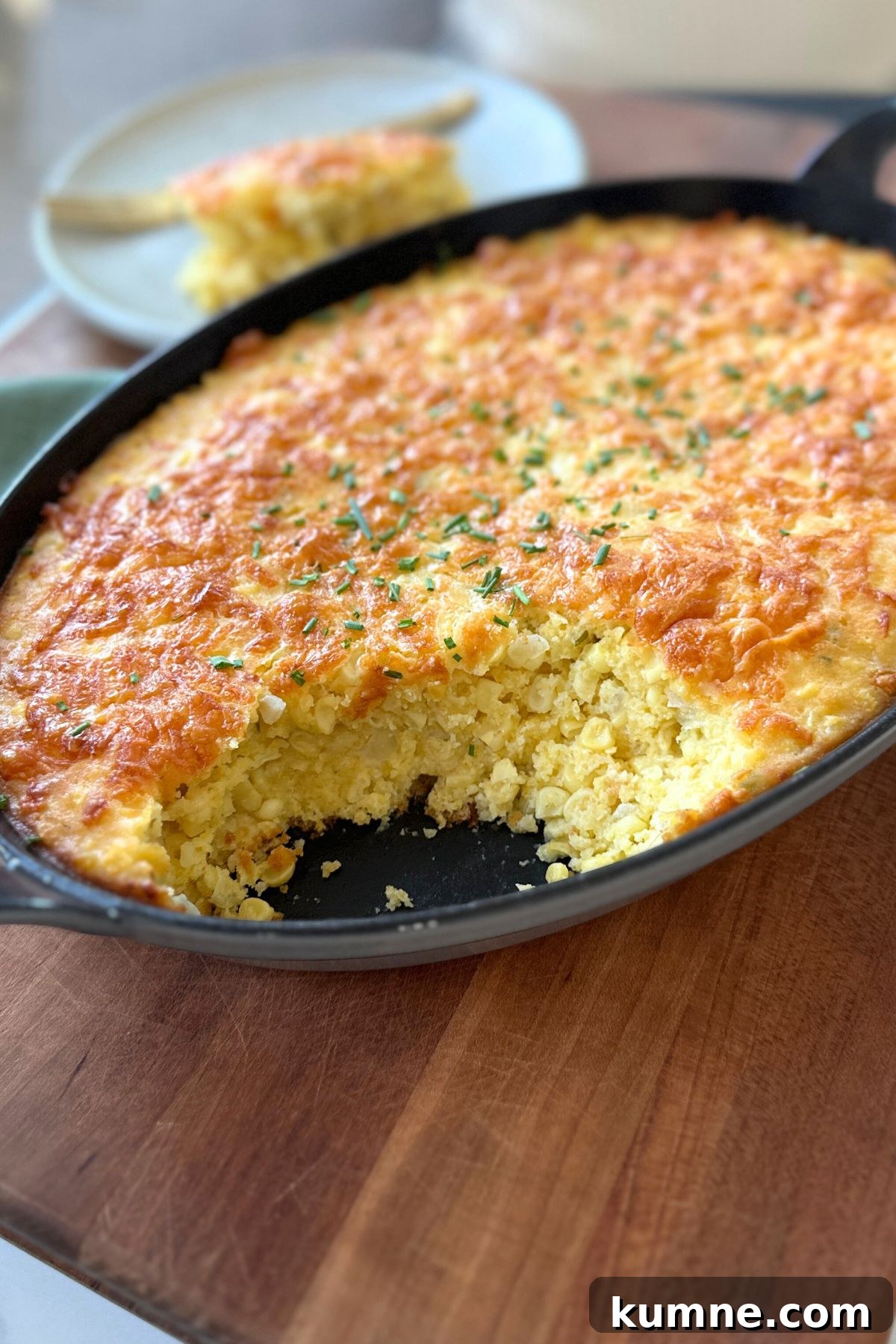 Creamy Baked Jalapeño Cheddar Corn Pudding Recipe from Scratch 11 Golden corn pudding baked in a black dish with corner slices cut out, served with a plated portion beside it.