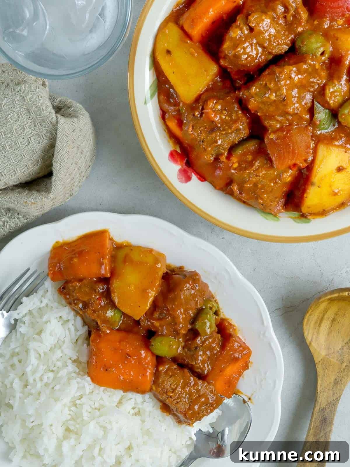 Beef Caldereta with white rice on a white plate with spoon and fork