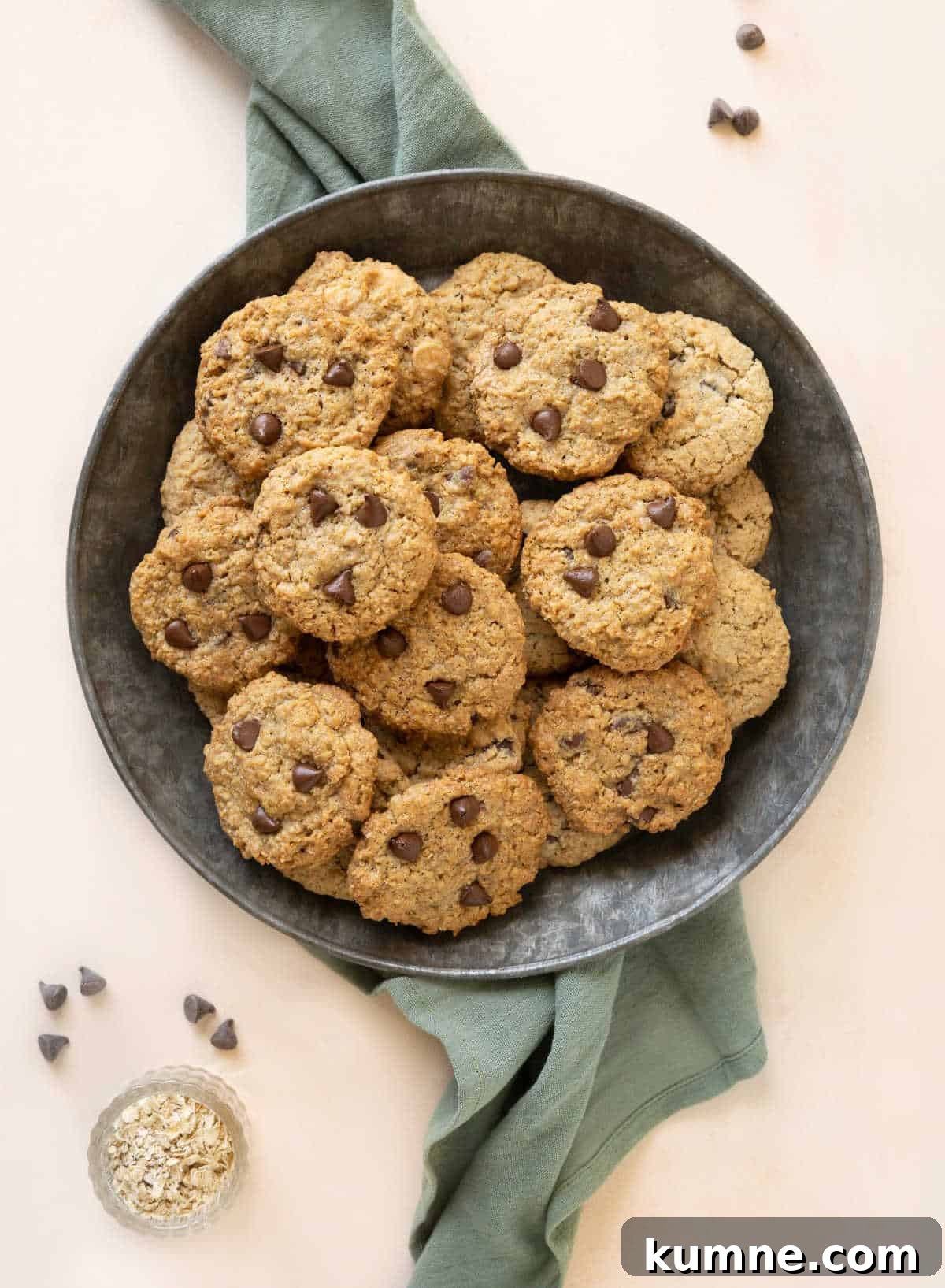 Chewy Chocolate Chip Oatmeal Cookies Recipe for Homemade Treats 2 Tin plate with pile of chocolate chip cookies on a light orange surface with a green cloth.