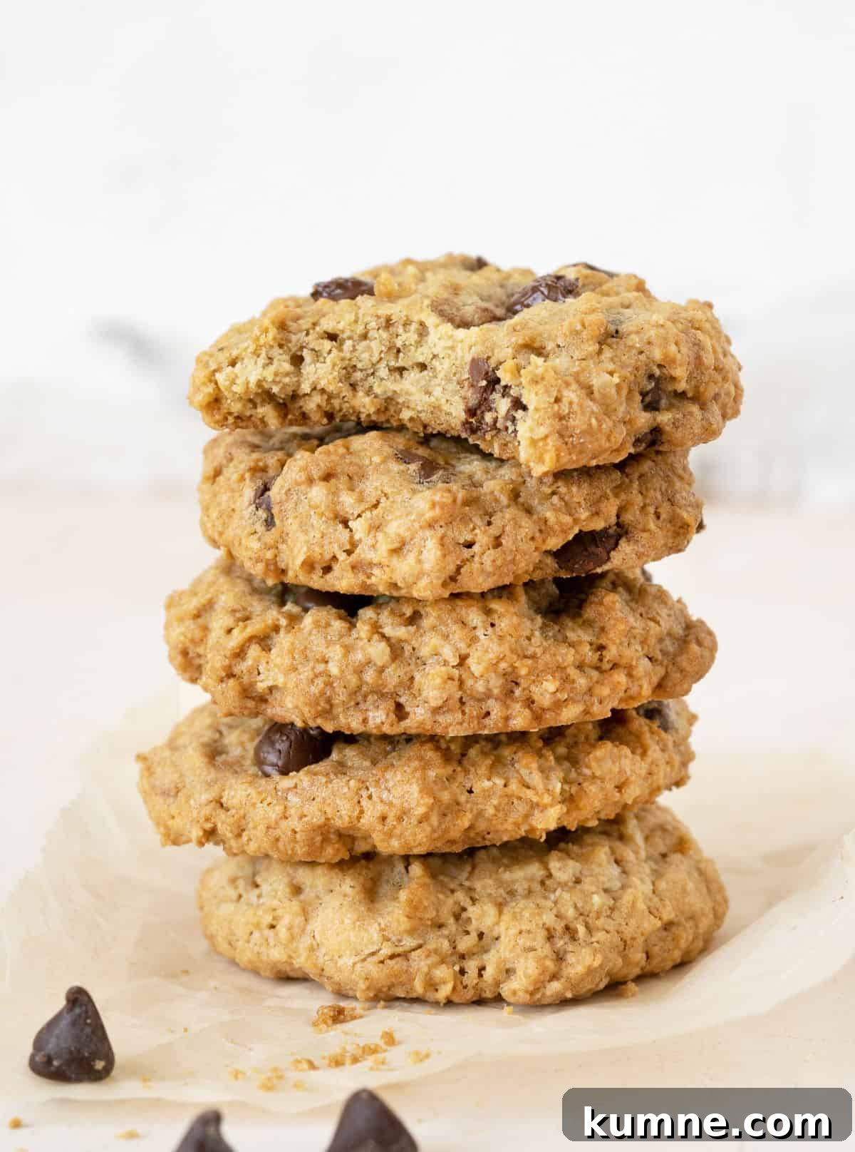 Chewy Chocolate Chip Oatmeal Cookies Recipe for Homemade Treats 8 Stack of chocolate chip oatmeal cookies on white and beige surface and background. Top one is bitten.