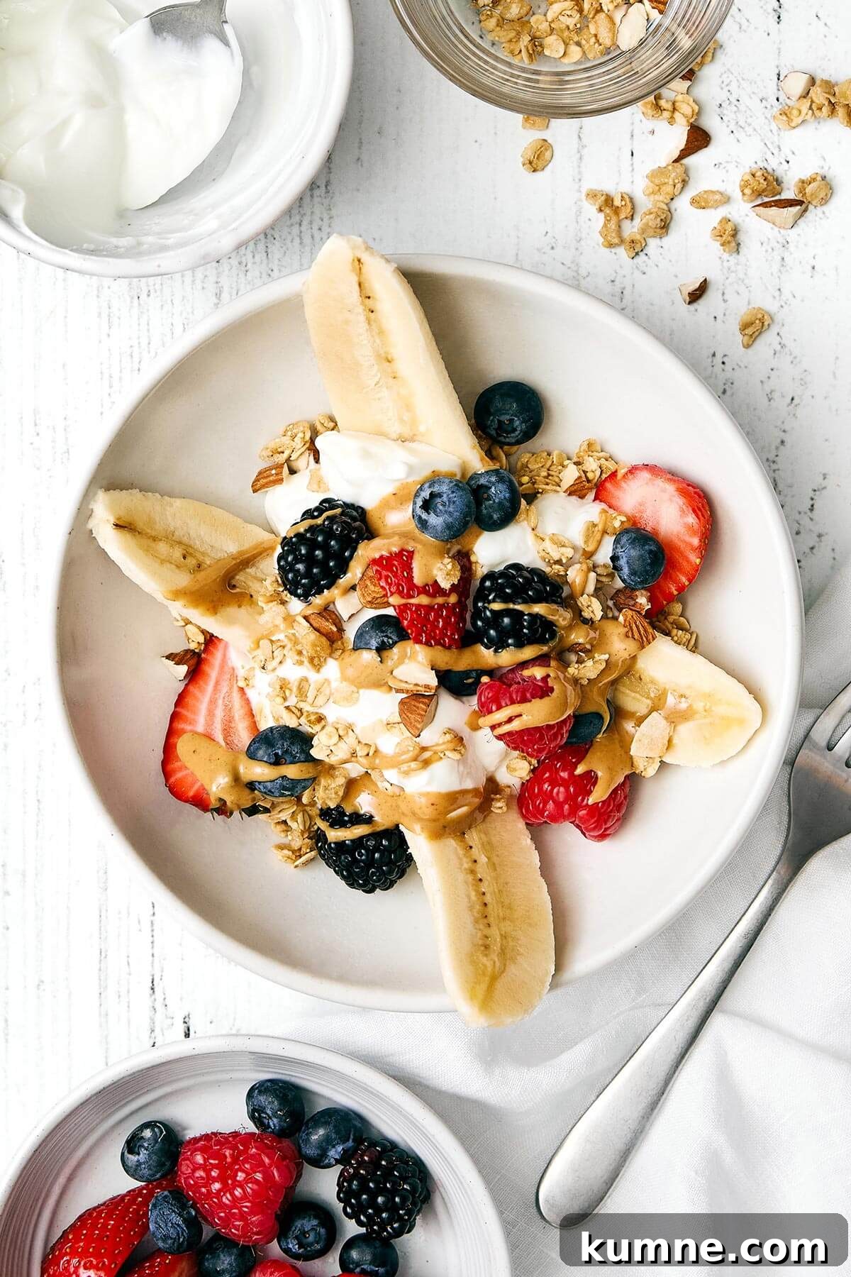 A breakfast banana split in a bowl next to toppings.