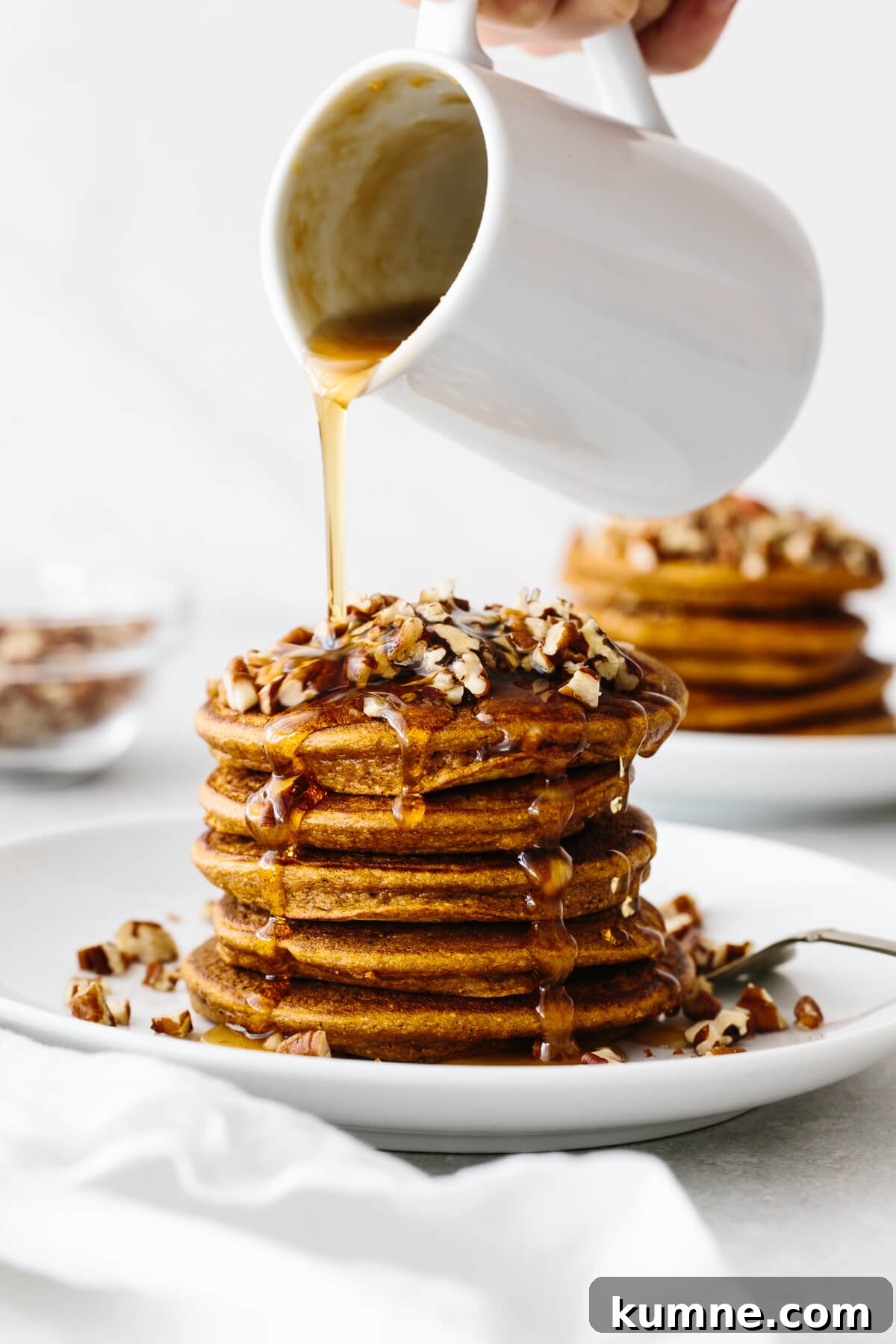 A stack of paleo pumpkin pancakes drizzled with maple ginger syrup.