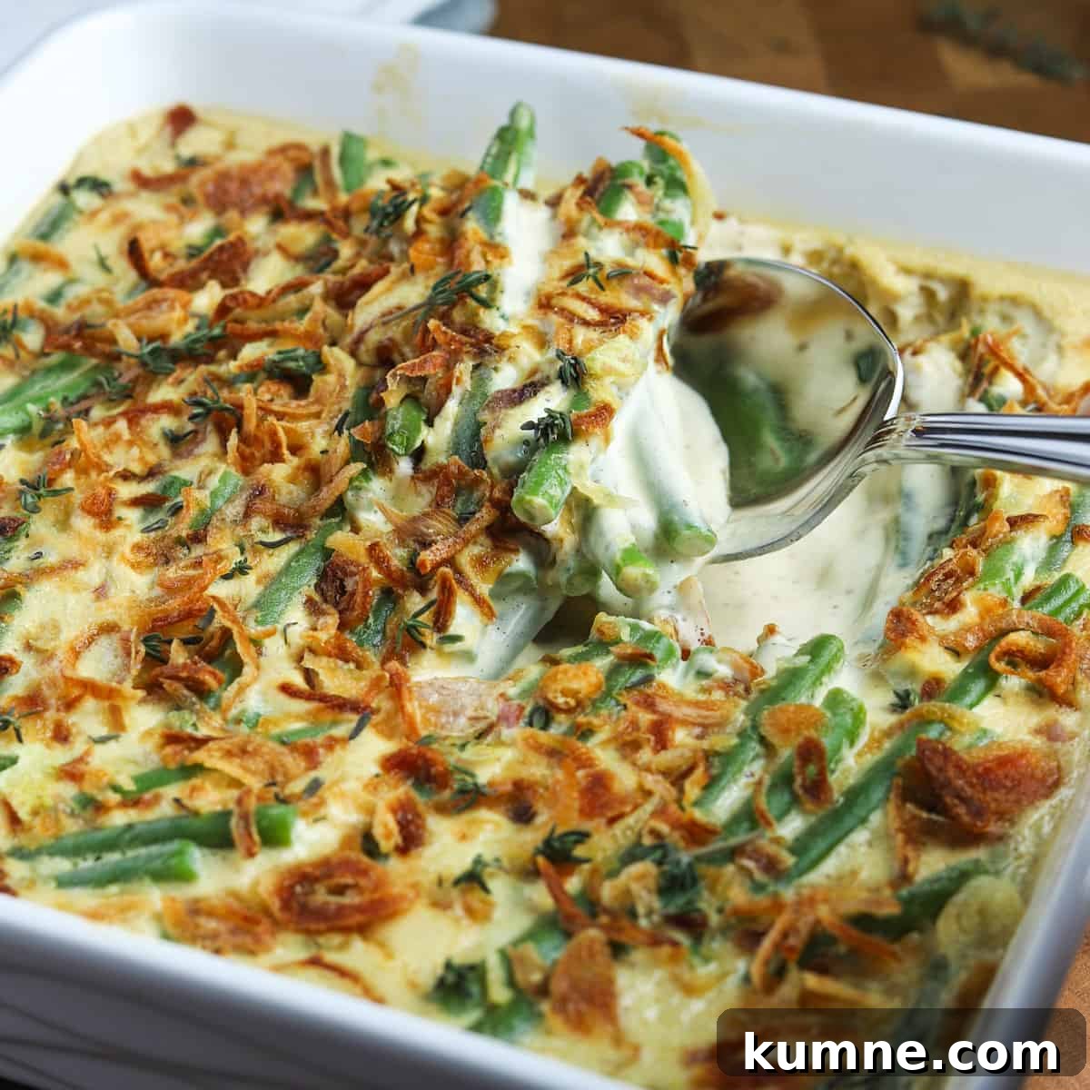 Photo of vegan green bean casserole in a square white ceramic dish with a spoon taking a portion out.