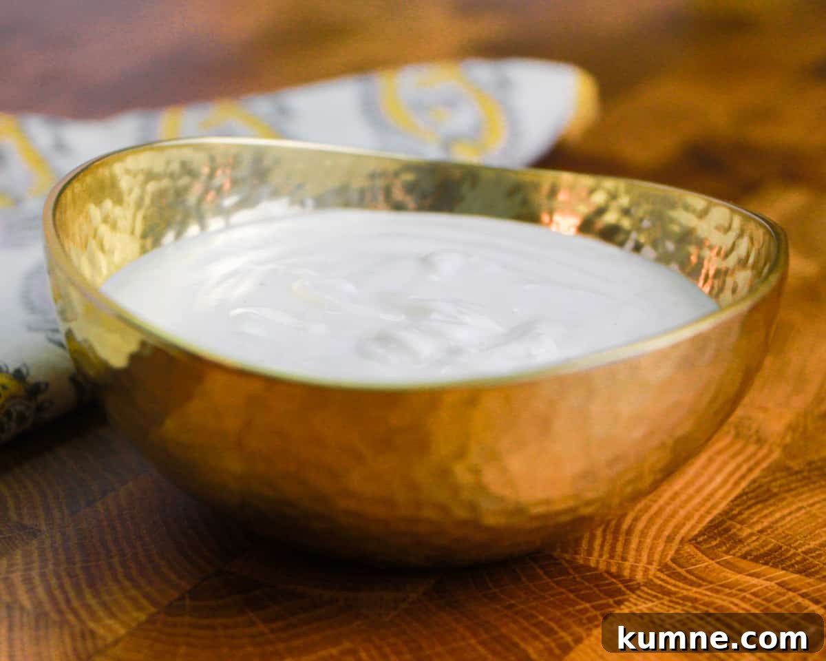 photo of a small brass bowl filled with cashew cream, on a wooden table top with a yellow patterned napkin in the background.