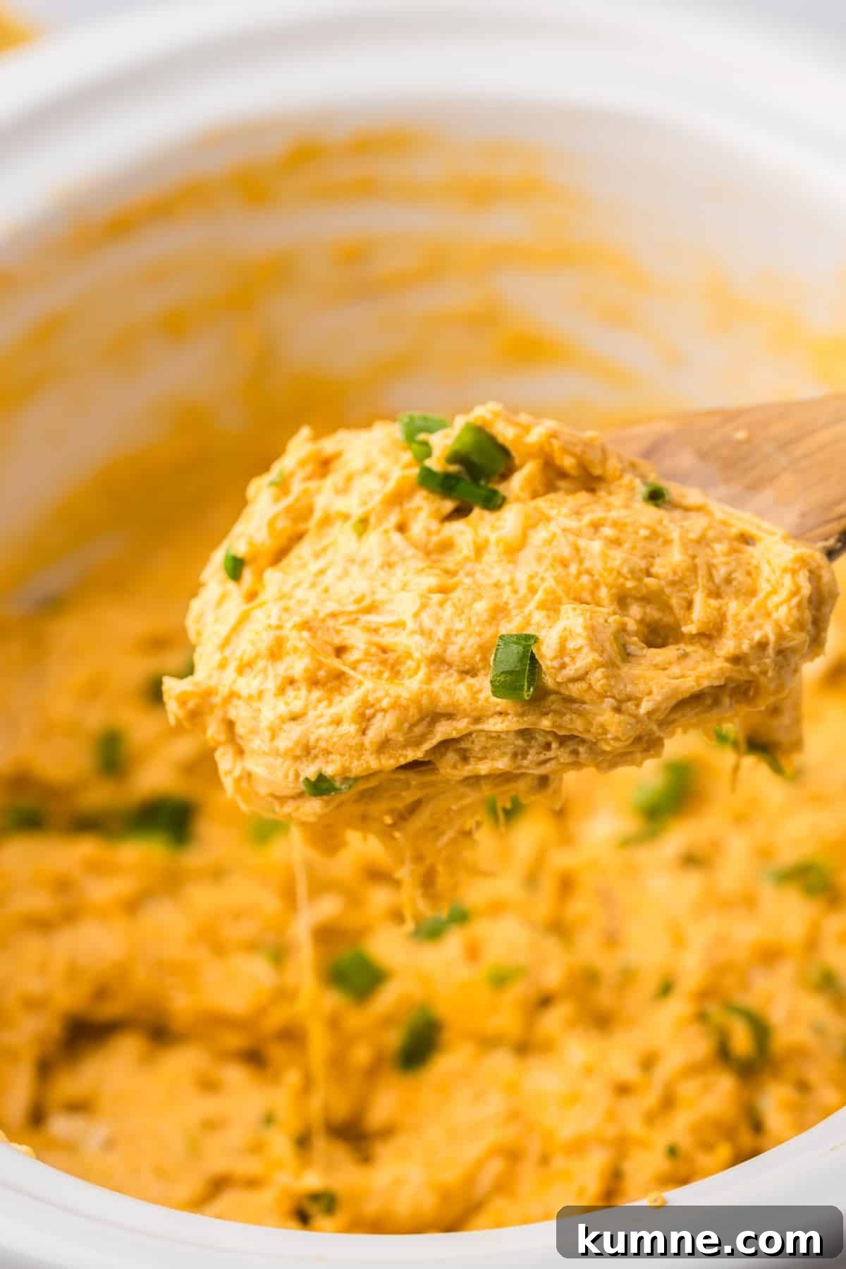 Slow Cooker Buffalo Chicken Dip Recipe for Game Day Snacks 14 A wooden spoon taking a small amount of chicken dip from a white slow cooker.