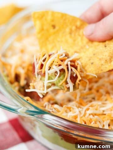 A tortilla chip dunking into a 4 layer dip.