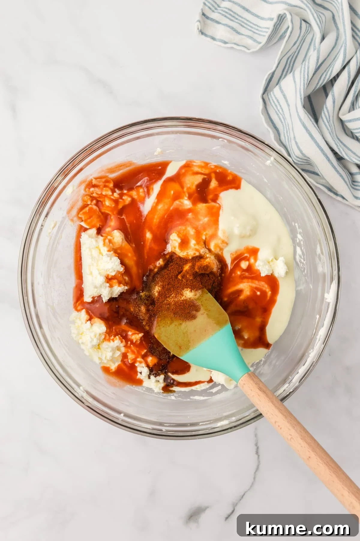 Slow Cooker Buffalo Chicken Dip Recipe for Game Day Snacks 5 A glass bowl filled with a cream cheese mixture, with cayenne pepper sauce inside.