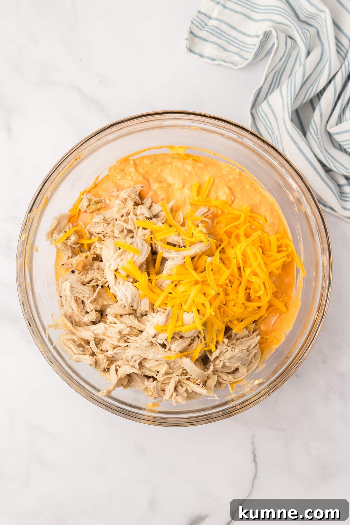 Slow Cooker Buffalo Chicken Dip Recipe for Game Day Snacks 7 A bowl filled with a dip mixture, with shredded cheese and cooked chicken on top.