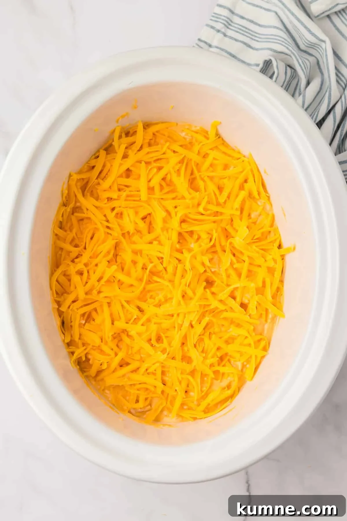 Slow Cooker Buffalo Chicken Dip Recipe for Game Day Snacks 9 A white crock pot with a cheesy dip inside, topped with shredded cheddar cheese.