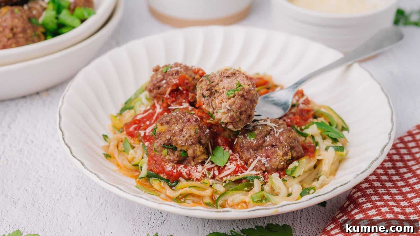 A plate of zucchini noodles topped with tomato sauce, meatballs, and grated cheese, garnished with parsley. A fork rests on the plate.