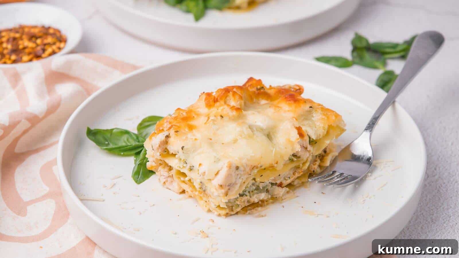 A slice of lasagna on a white plate, garnished with basil leaves, and a fork beside it.