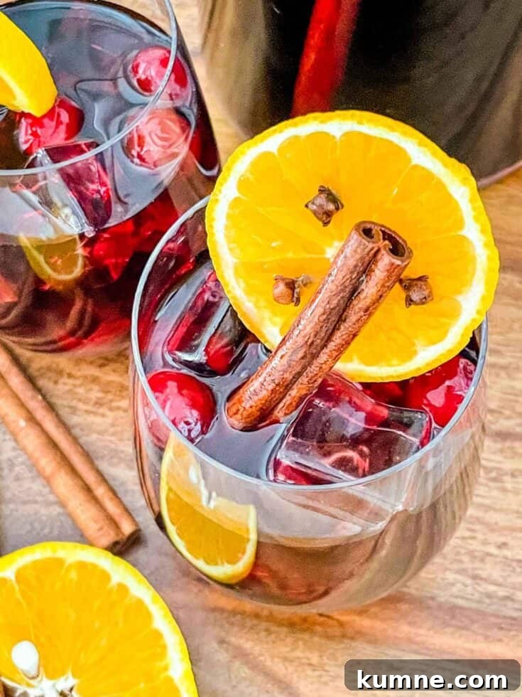 A glass of cranberry orange holiday red wine sangria garnished with cinnamon and orange.
