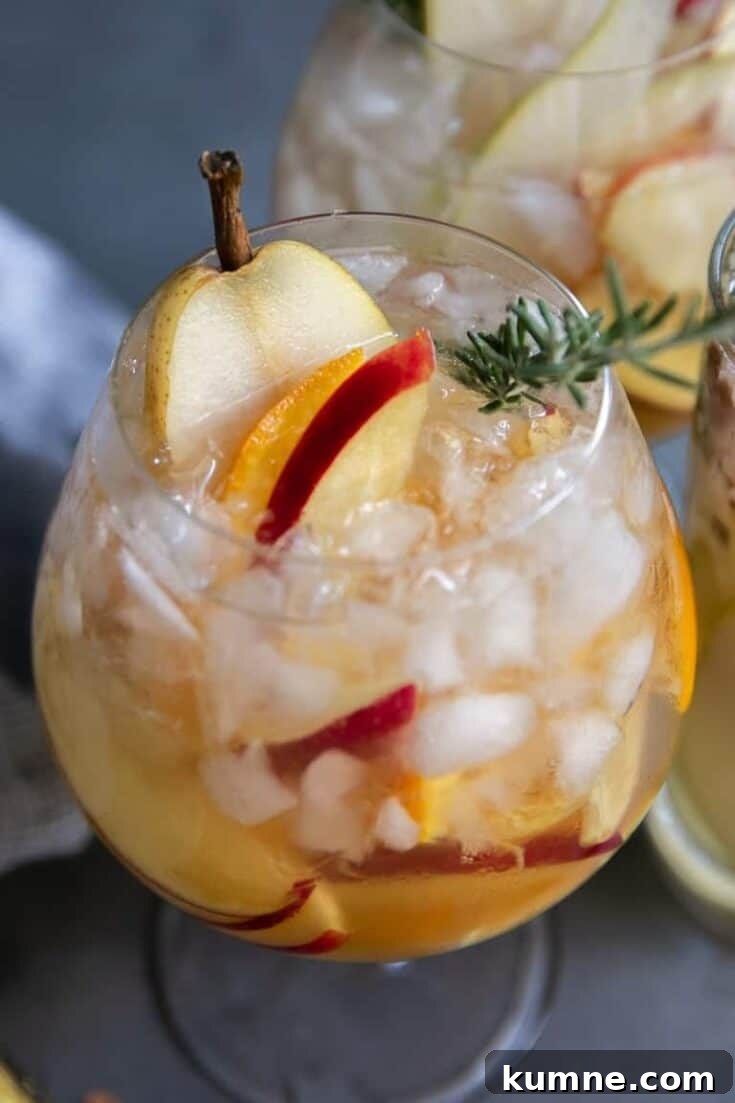 A glass of white fall sangria made with apples, pear and rosemary.
