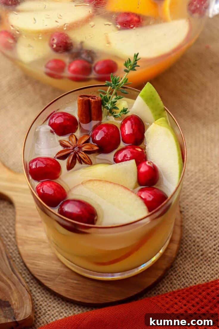 A glass of autumn harvest sangria garnished with cranberries and apples.