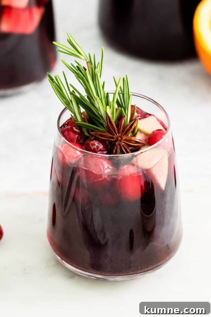 A glass of red wine sangria garnished with rosemary.
