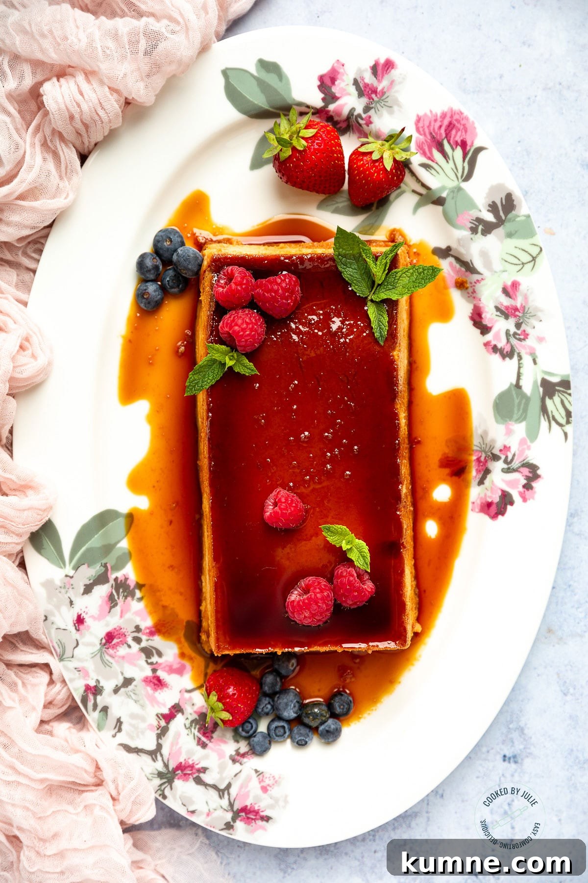 flan with caramel, berries, and fresh mint on a white platter with a pink towel on the side.