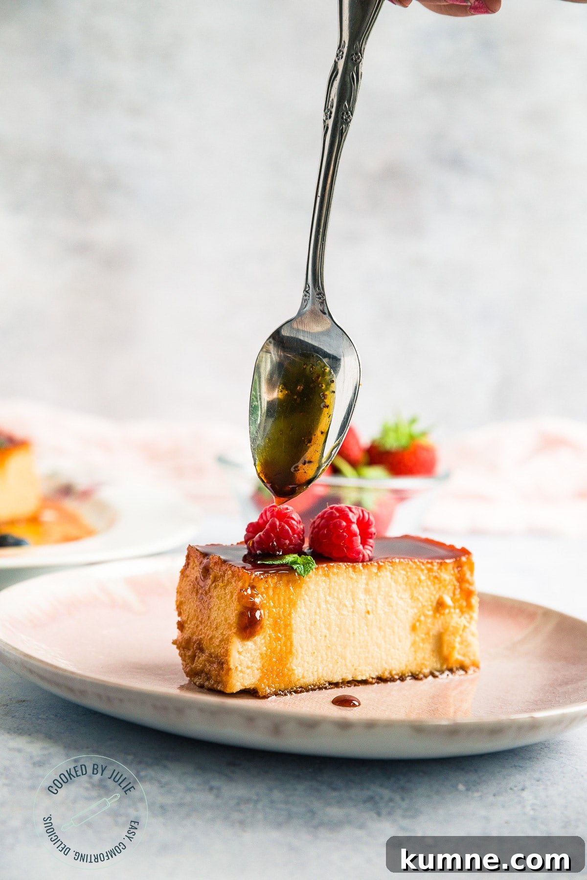 a slice of caramel custard on a pink plate with a spoon drizzling caramel over it.