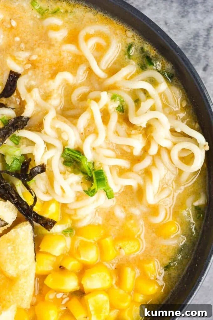 Quick 15-Minute Vegan Miso Ramen Recipe 6 A close up top down view of a dark grey bowl with a creamy pale broth and noodles, tofu puffs and sweetcorn