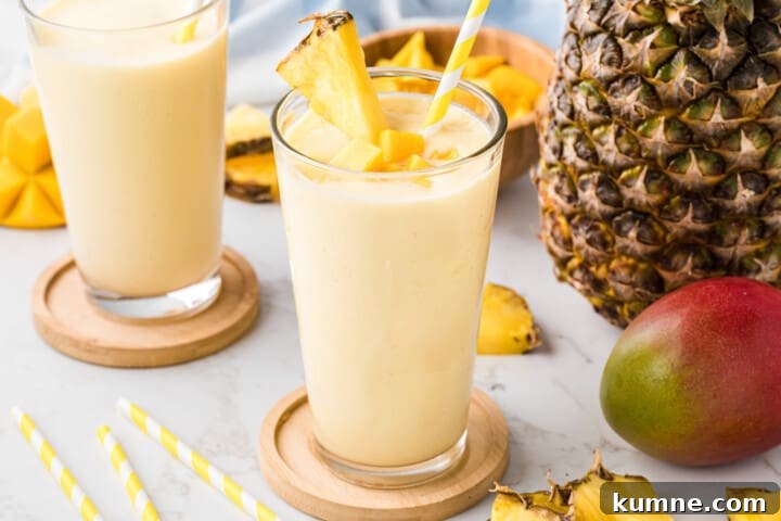 Creamy Mango Pineapple Smoothie Recipe for Tropical Refreshment 5 two smoothies in a glass on wooden coasters.