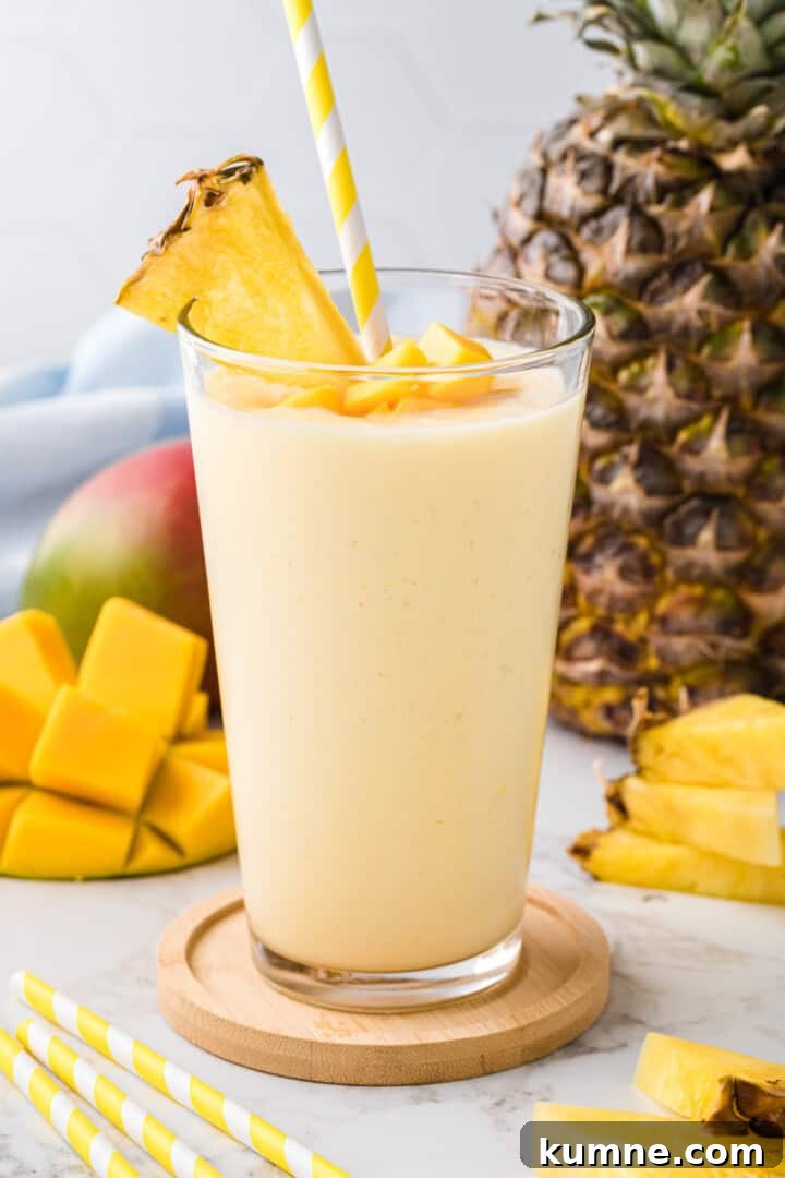 Creamy Mango Pineapple Smoothie Recipe for Tropical Refreshment 8 Mango Pineapple Smoothie in glass garnished with mangoes and pineapple slice.
