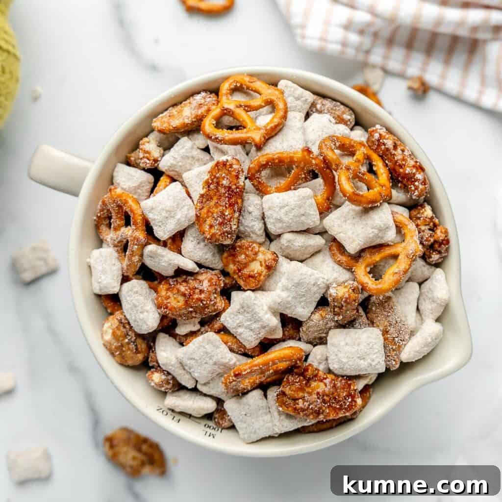 A bowl filled with powdered sugar-coated cereal pieces, candied nuts, and mini pretzels on a marble surface.
