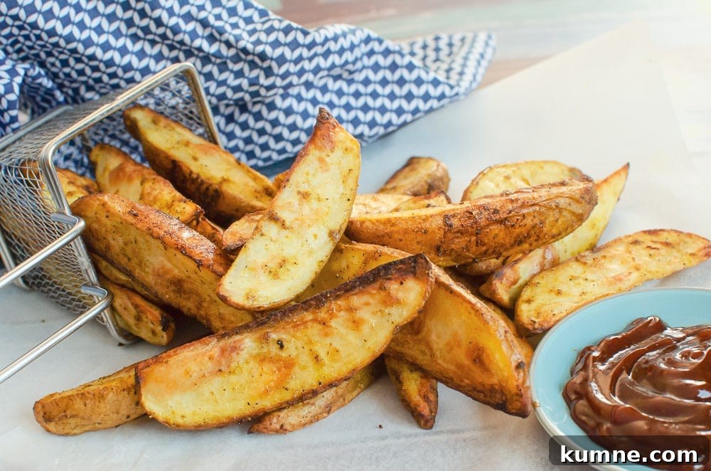 spicy curried potato wedges pouring out of a silver fry basket on white parchment paper with bbq sauce on the side