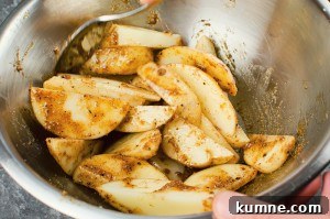 Mixing the potato wedges in the spicy mixture in a silver mixing bowl