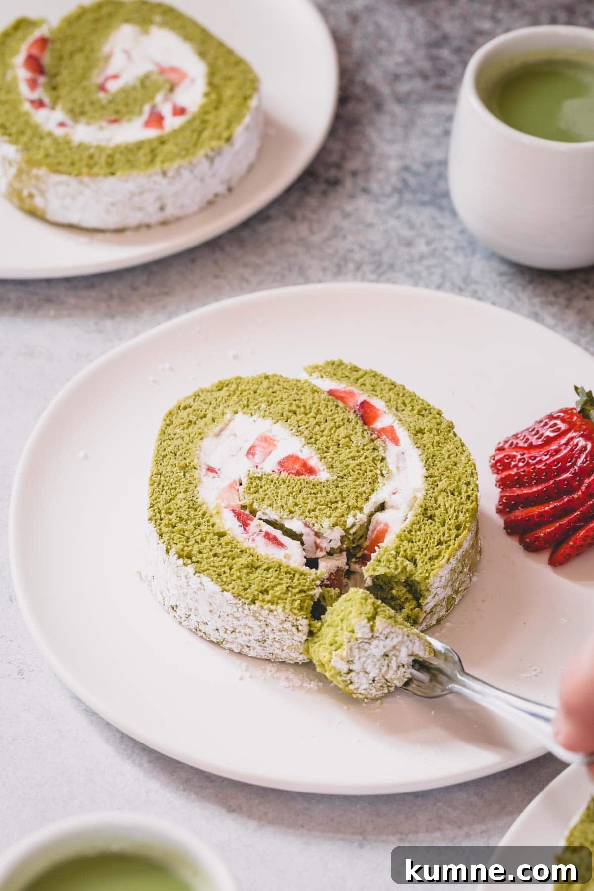Matcha Swiss Roll Cake Recipe — Light, Fluffy Japanese Roll 2 A slice of strawberry matcha roll cake on a white serving plate with a a little slice cut with a fork.