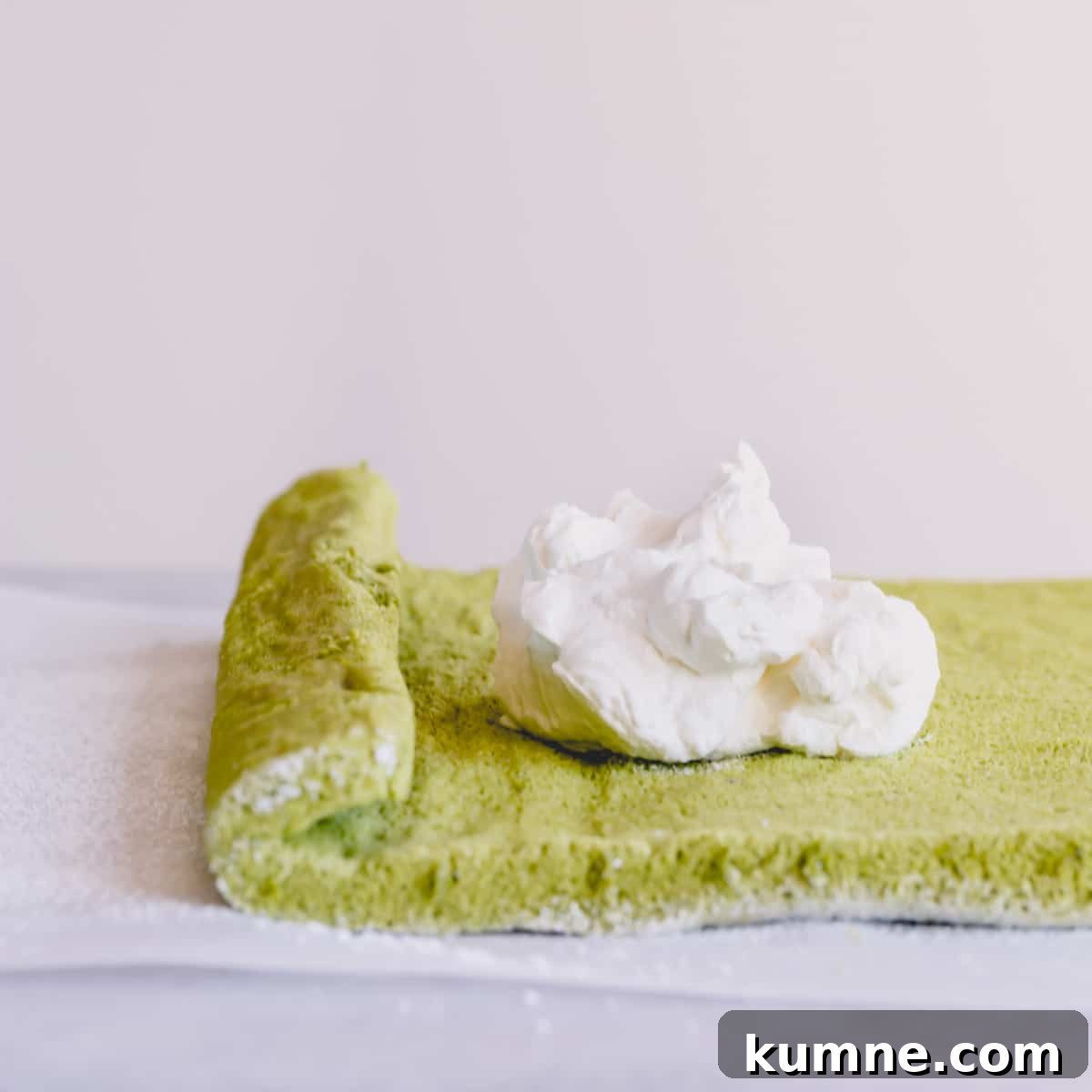 Matcha Swiss Roll Cake Recipe — Light, Fluffy Japanese Roll 6 Green sponge cake on a parchment paper with a big dollop of whipped cream in the middle.