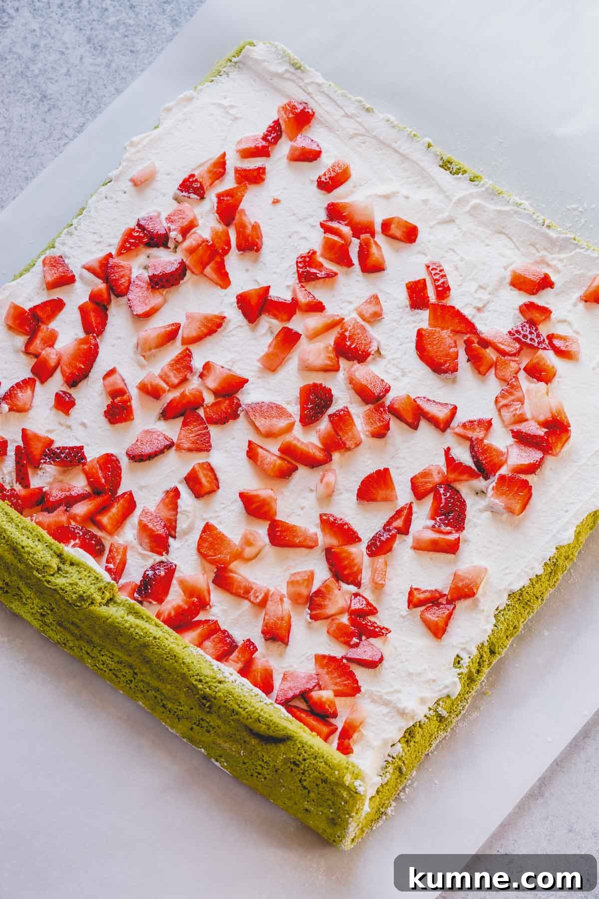 Matcha Swiss Roll Cake Recipe — Light, Fluffy Japanese Roll 7 Sheet of green sponge cake with whipped cream spread all over and diced strawberries scattered over the cream.