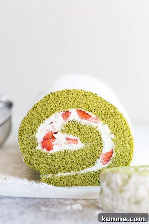 Matcha Swiss Roll Cake Recipe — Light, Fluffy Japanese Roll 3 Strawberry matcha roll cake with small sieve next to it.