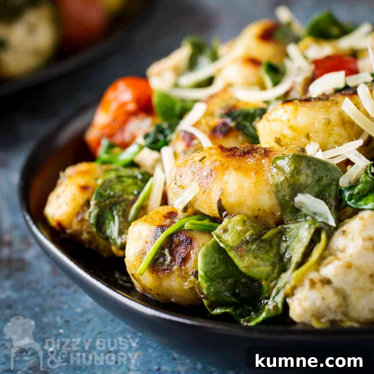 Side close up shot of pesto chicken and gnocchi sprinkled with shredded parmesan on a black plate.