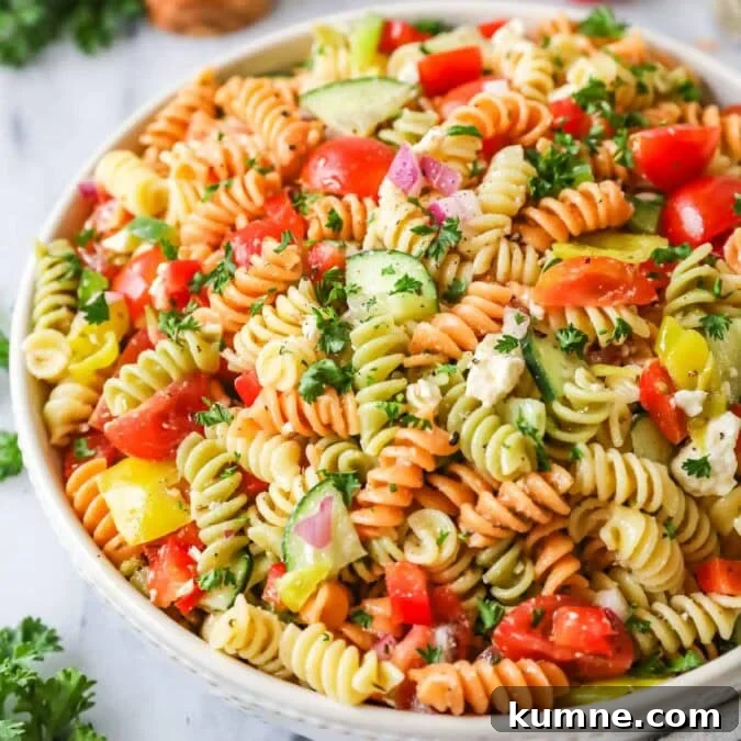 Bowl of pasta salad made with tri-color rotini, veggies, and feta cheese.