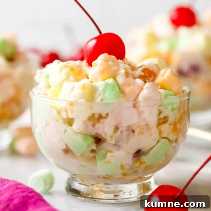 Glass bowl of ambrosia salad topped with a maraschino cherry.