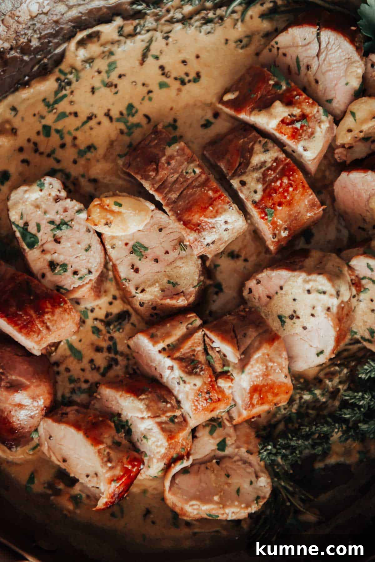 Pork tenderloin in a pan with sauce and herbs.