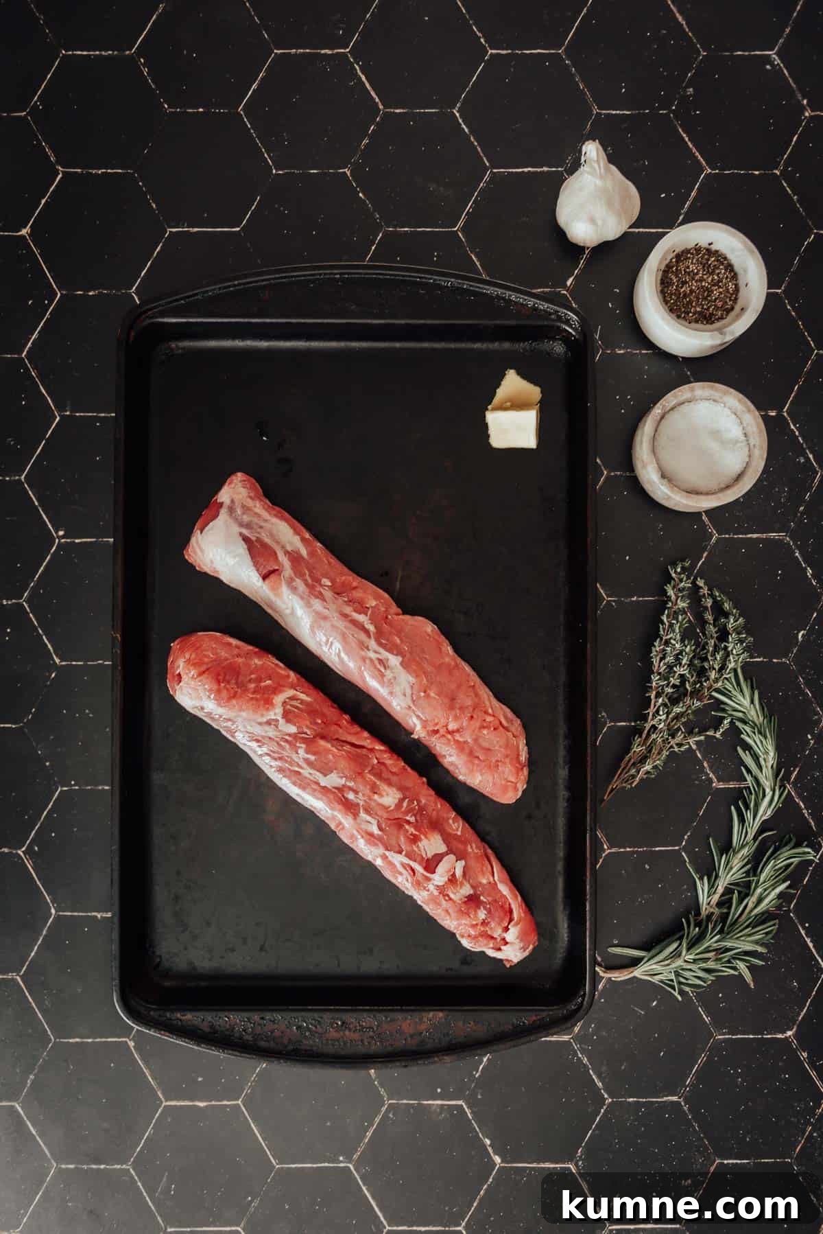 Two pork tenderloins on a tray with herbs and spices.