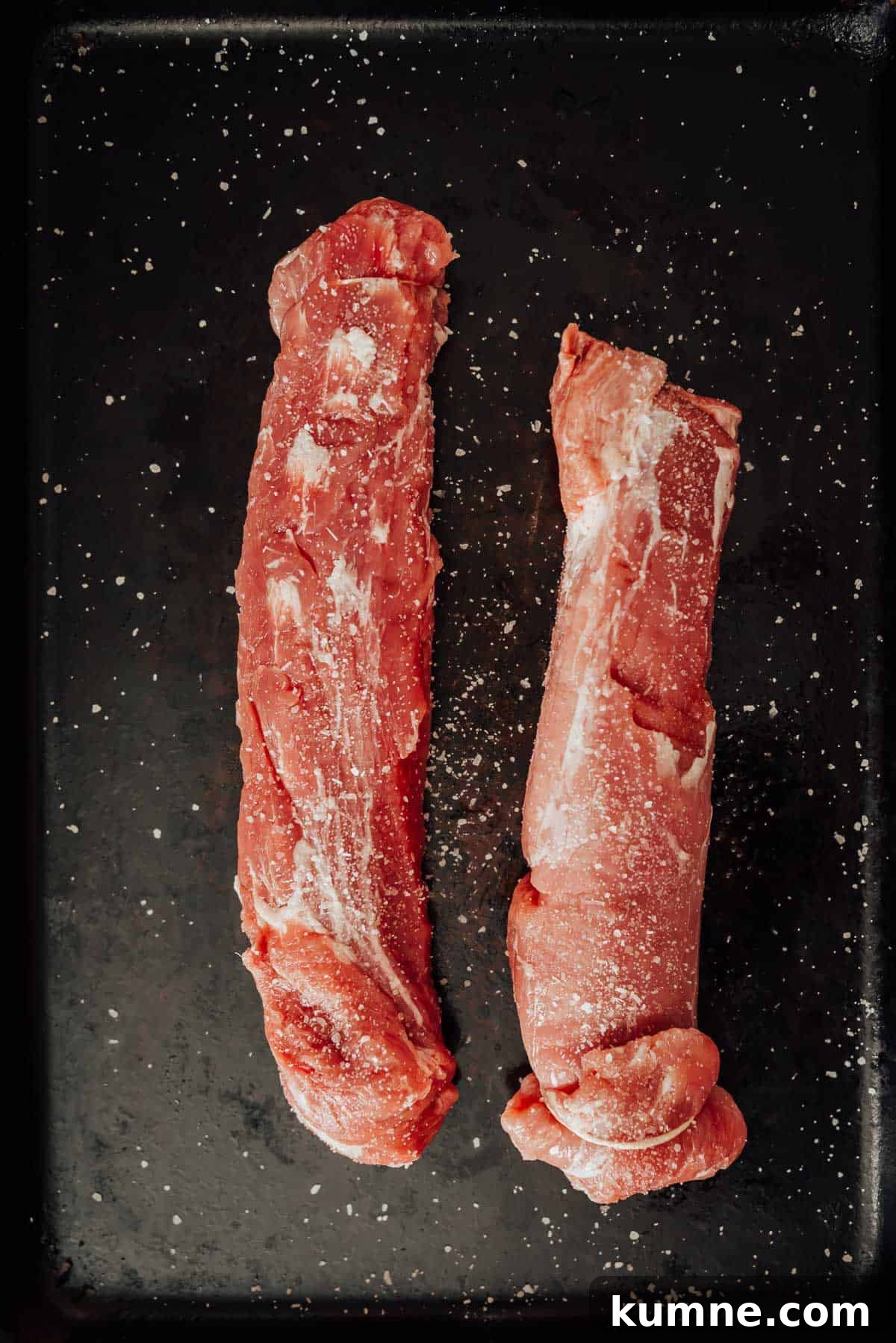 Two pork tenderloins on a black tray.