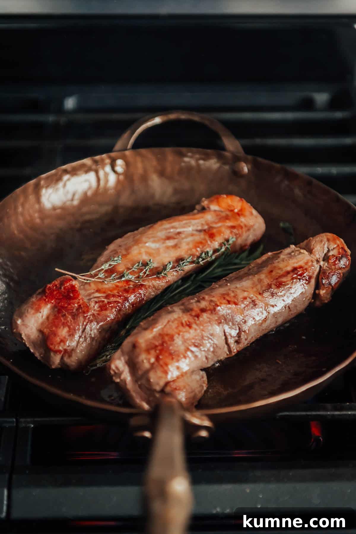 Two pork tenderloins in a frying pan on a stove.