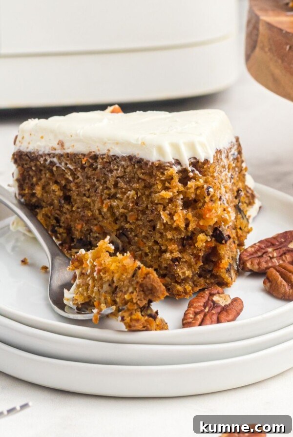 Slice of carrot cake on a white plate with a fork holding a bite of the cake
