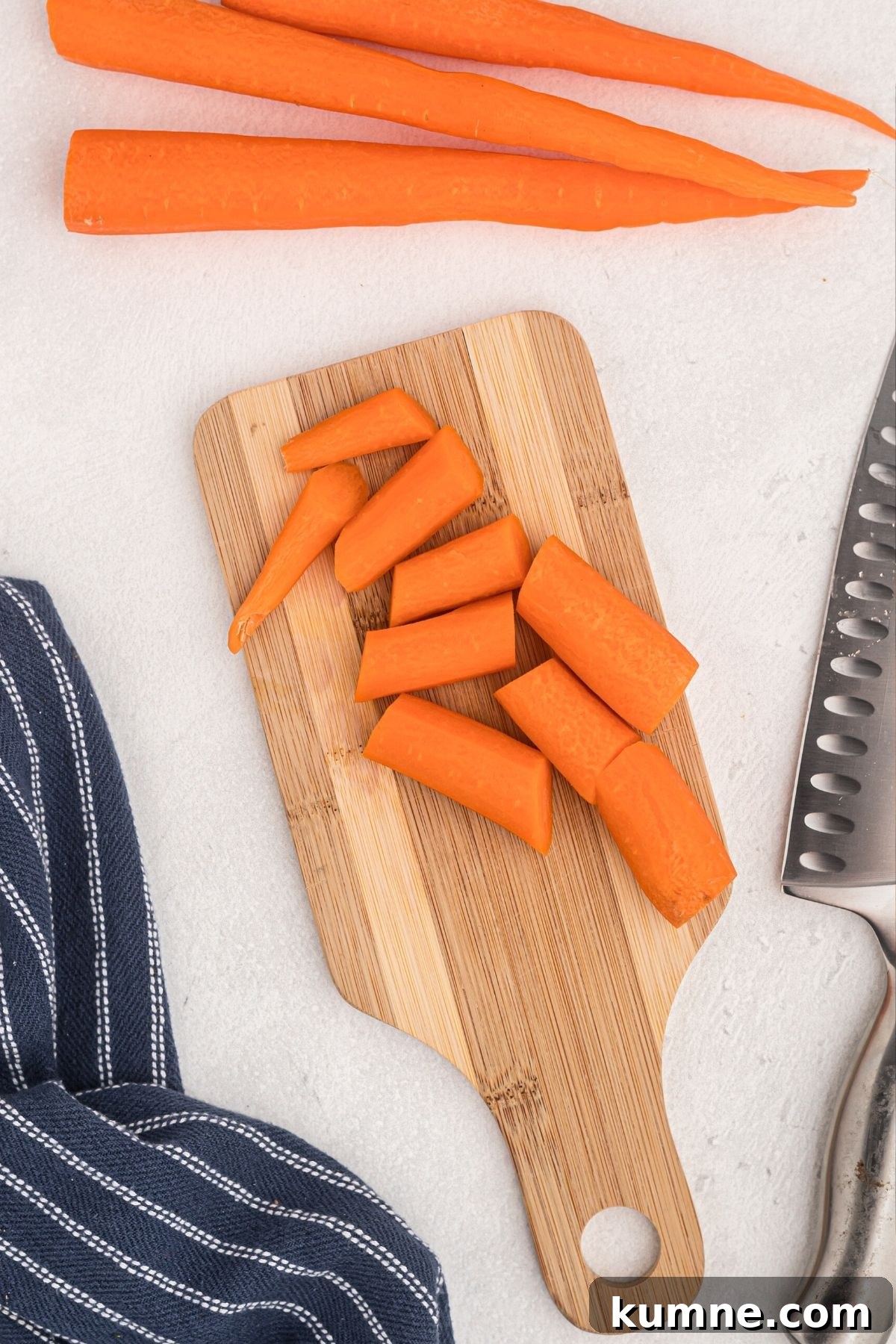 Carrots being sliced on a wooden cutting board with a knife