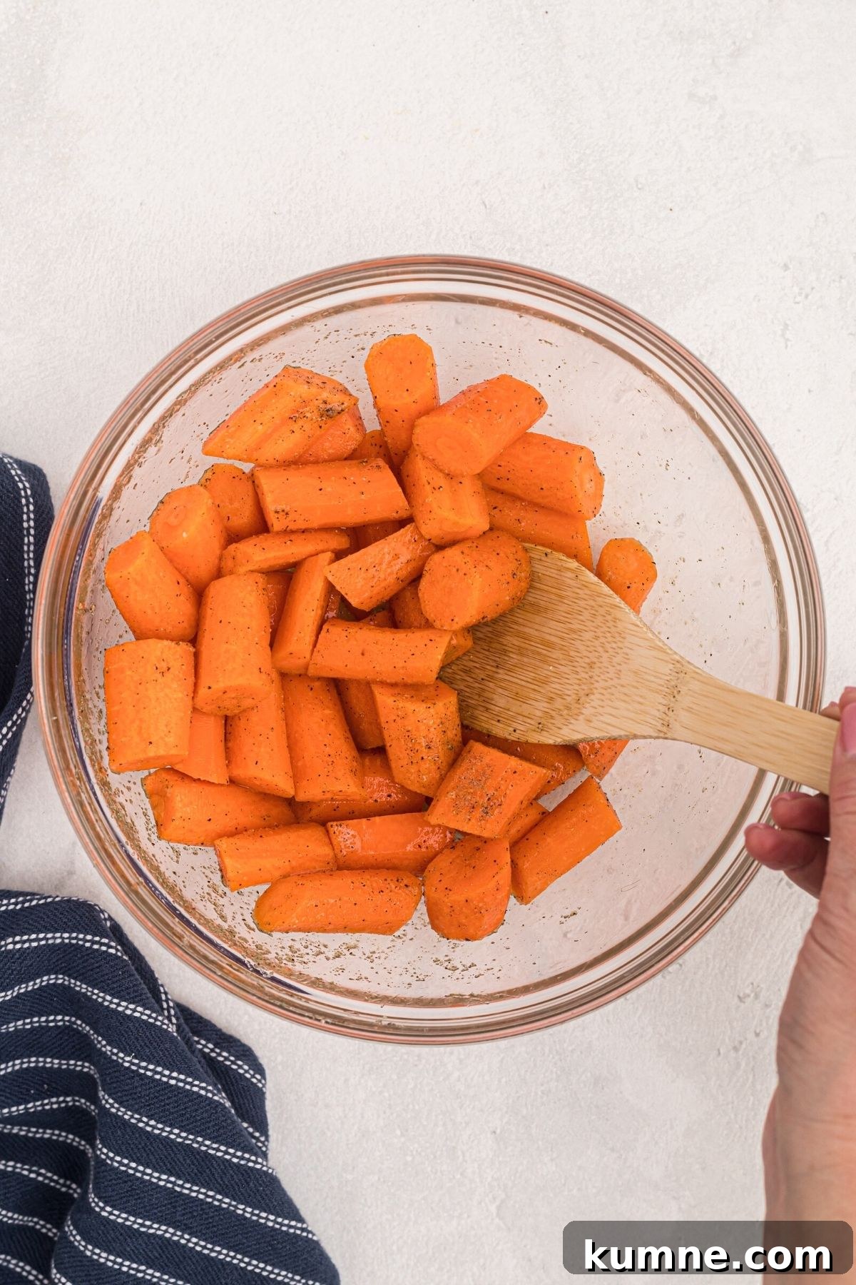 Carrots being tossed with olive oil and seasonings in a clear glass bowl