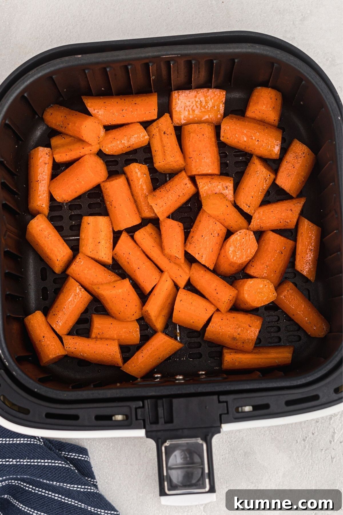 Uncooked chopped carrots in the air fryer basket after being seasoned