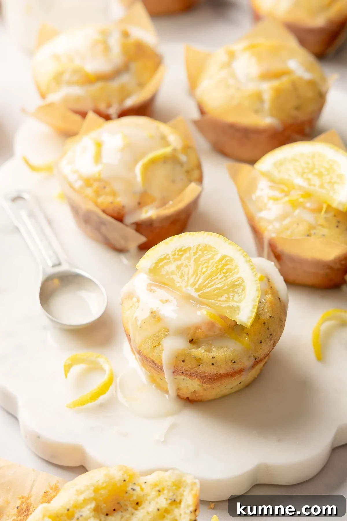 Gluten-Free Lemon Poppy Seed Muffins Recipe for Moist, Zesty Bites 2 Glazed lemon poppy seed muffins topped with lemon slices, served on marble board with zest.