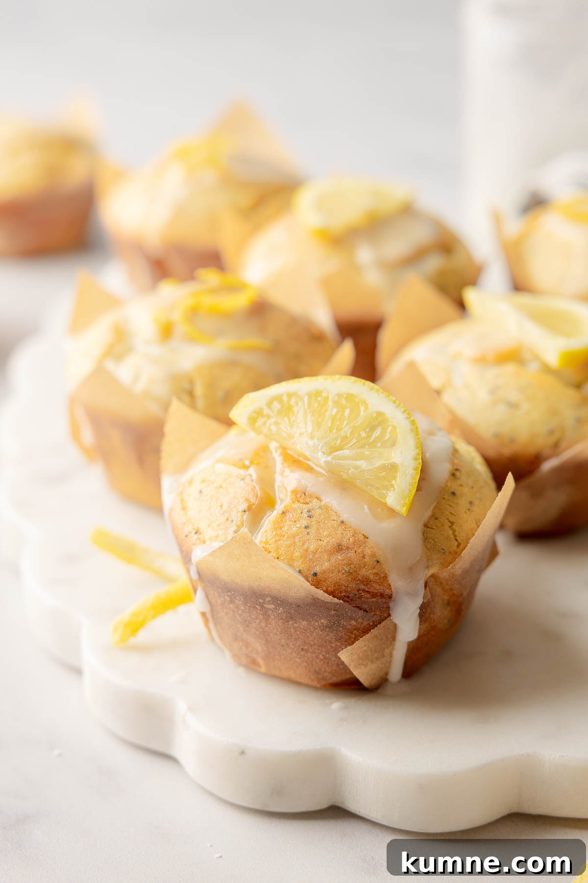 Gluten-Free Lemon Poppy Seed Muffins Recipe for Moist, Zesty Bites 6 Lemon poppy seed muffins with glaze and lemon slice garnish on marble board.