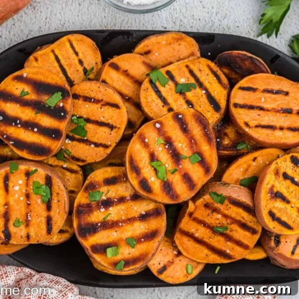 Crispy Foil-Grilled Potatoes with Garlic and Herbs 9 Sliced grilled sweet potatoes stacked on a black platter topped with chopped herbs.