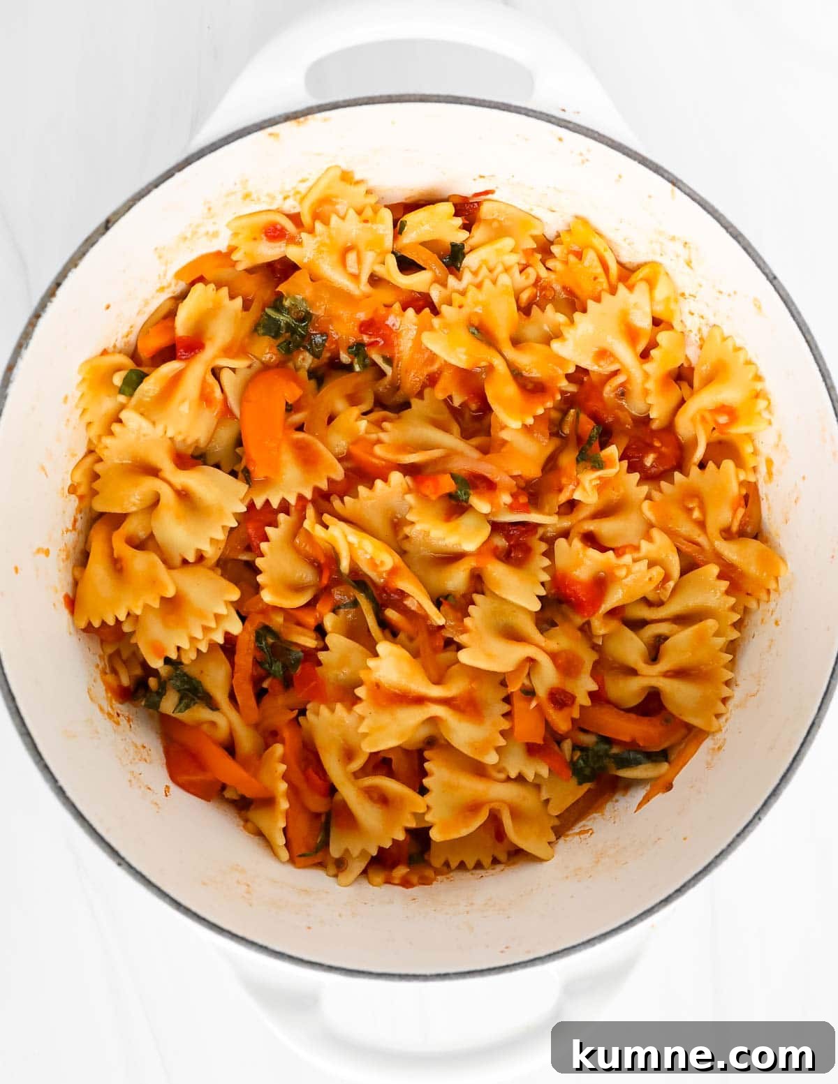 Pasta in a red sauce with vegetables in a large white pot.