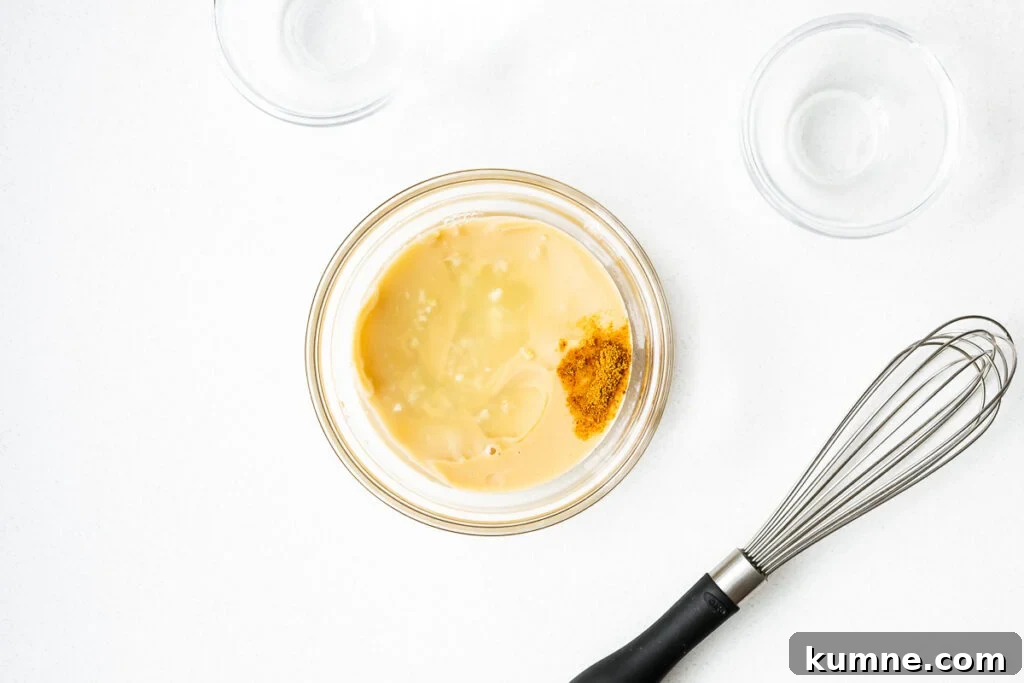 Tahini sauce ingredients in a small glass bowl next to an unused whisk.