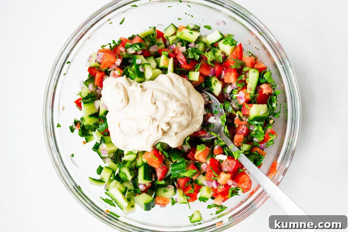 Israeli chopped salad (Jerusalem salad) topped with tahini sauce in a glass bowl before mixing.