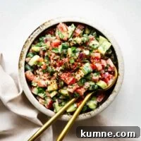 Jerusalem salad (Israeli salad) with tahini sauce in a bowl with golden serving spoons viewed from above.